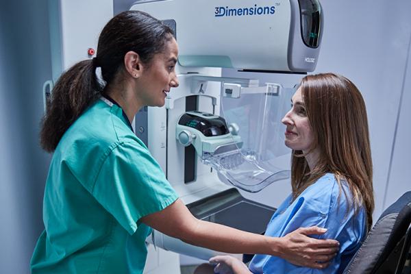 Vrouwen zitten voor een mammografieapparaat met een medisch zorgverlener aan hun zijde.