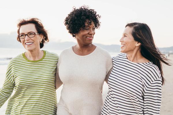 Drie vrouwen die lachend samen over het strand wandelen.