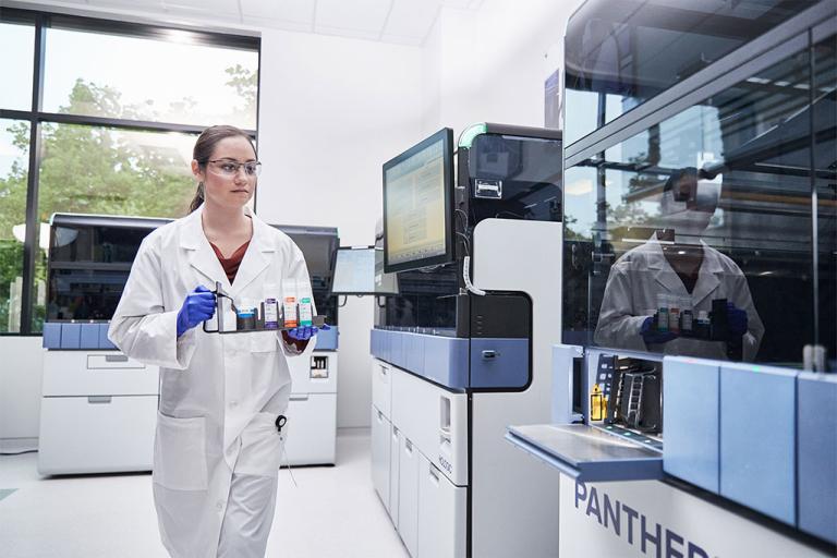 Vrouwelijke laborant draagt een schaal met monsters om in het Panther-systeem te plaatsen