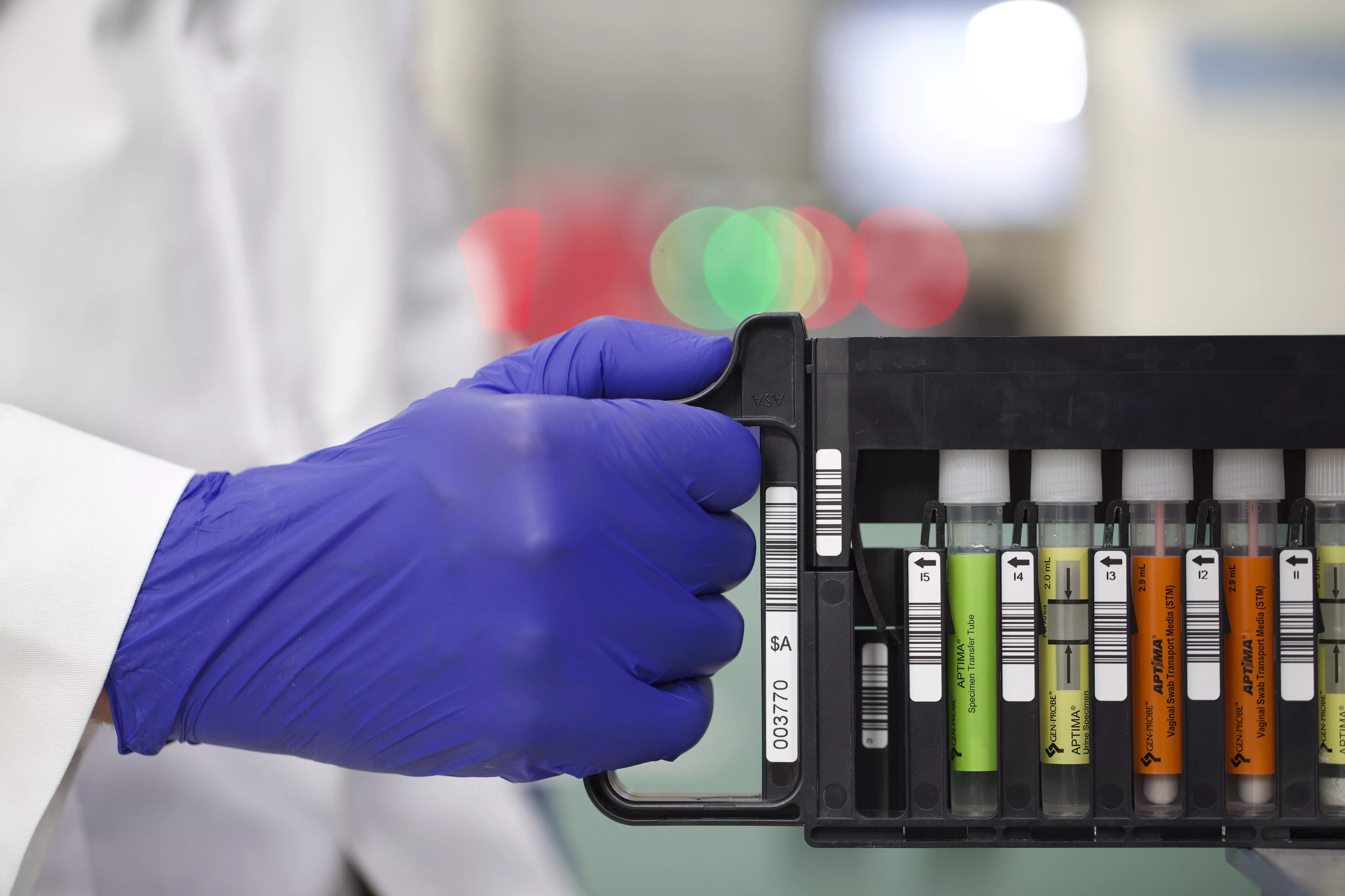 Hand met handschoen die een rekje met flacons vasthoudt in een laboratorium