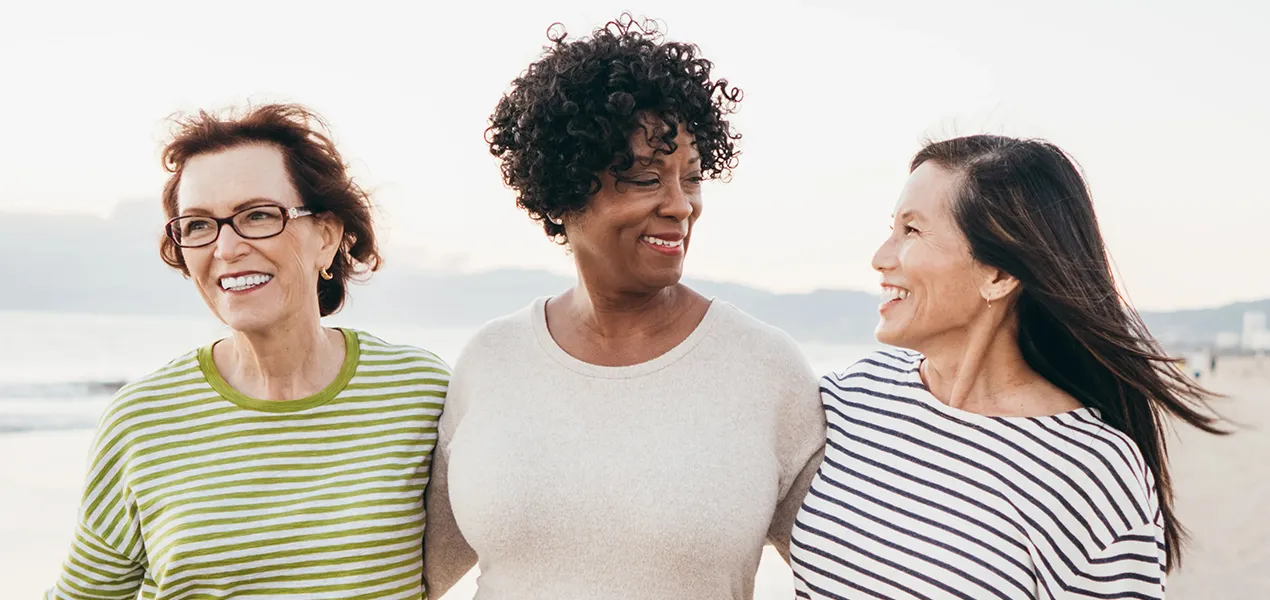 Drie vrouwen die lachend samen over het strand wandelen.
