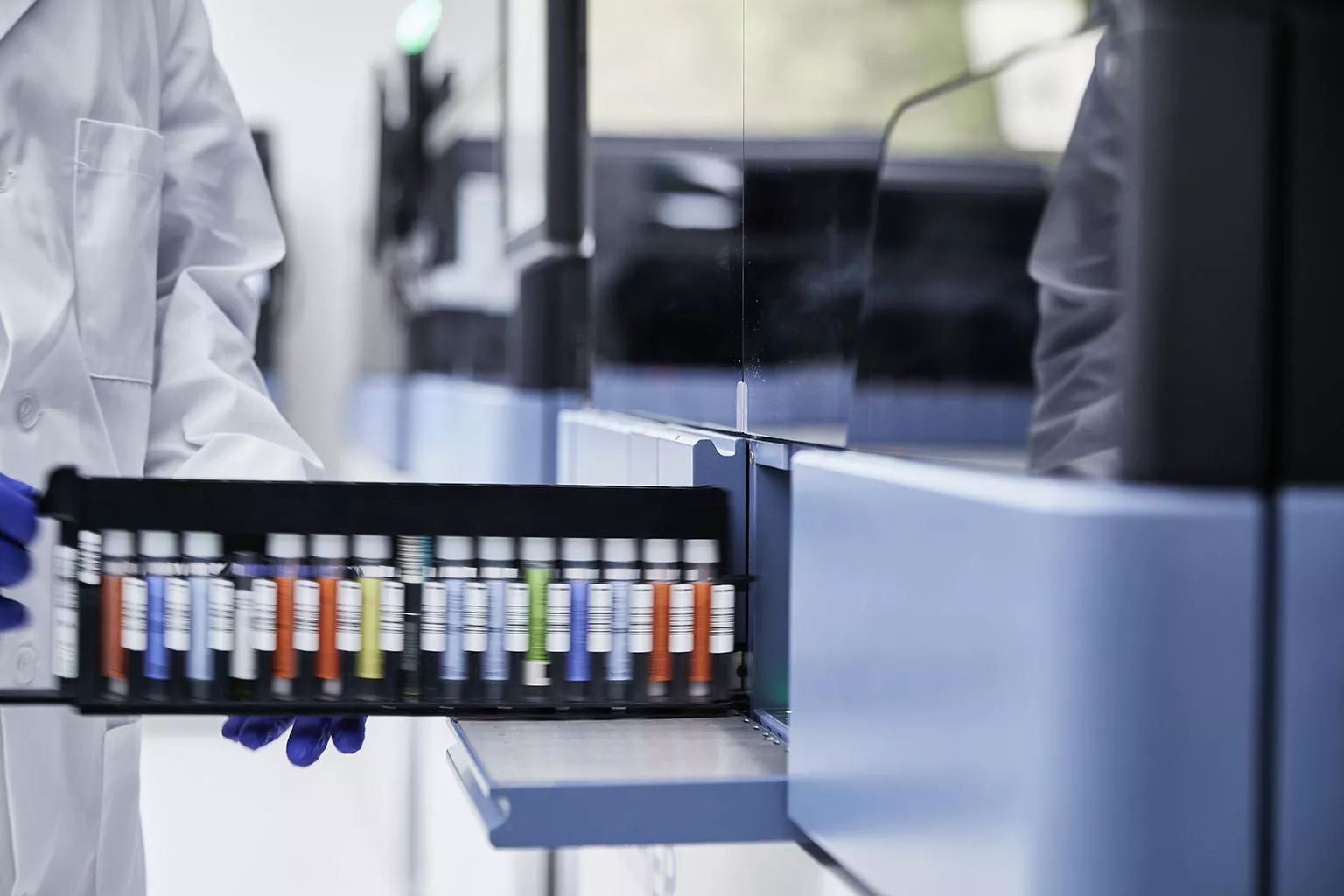 Hand met handschoen houdt rekje met flacons vast in laboratorium.