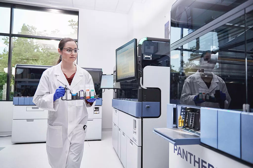 Laborant draagt een tray met monsters om in het Panther-systeem te plaatsen