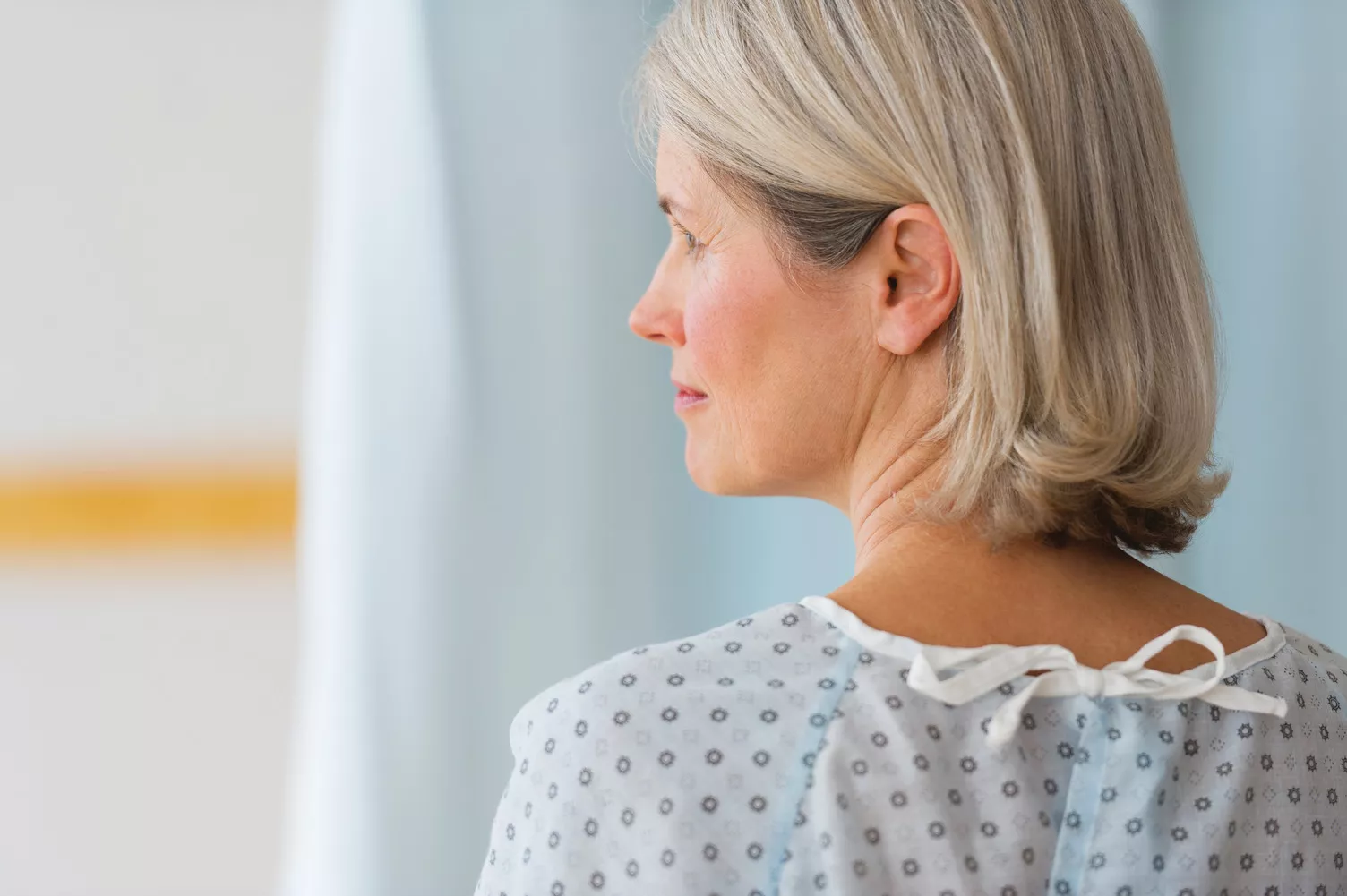 Bejaarde vrouw in patiëntjas kijkt naar links