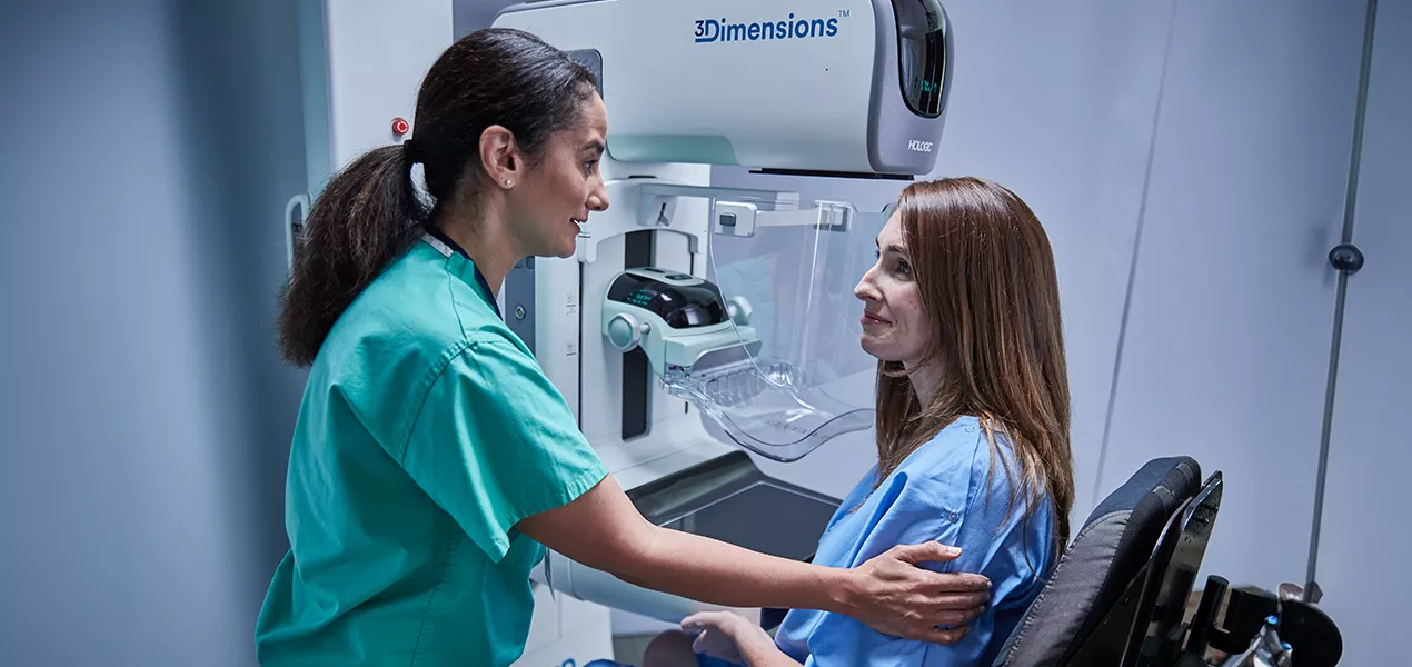 Vrouwen zitten voor een mammografieapparaat met een medisch zorgverlener aan hun zijde.