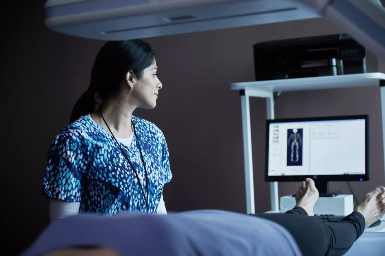 Zorgprofessional bekijkt scan op beeldscherm terwijl patiënt op bed ligt